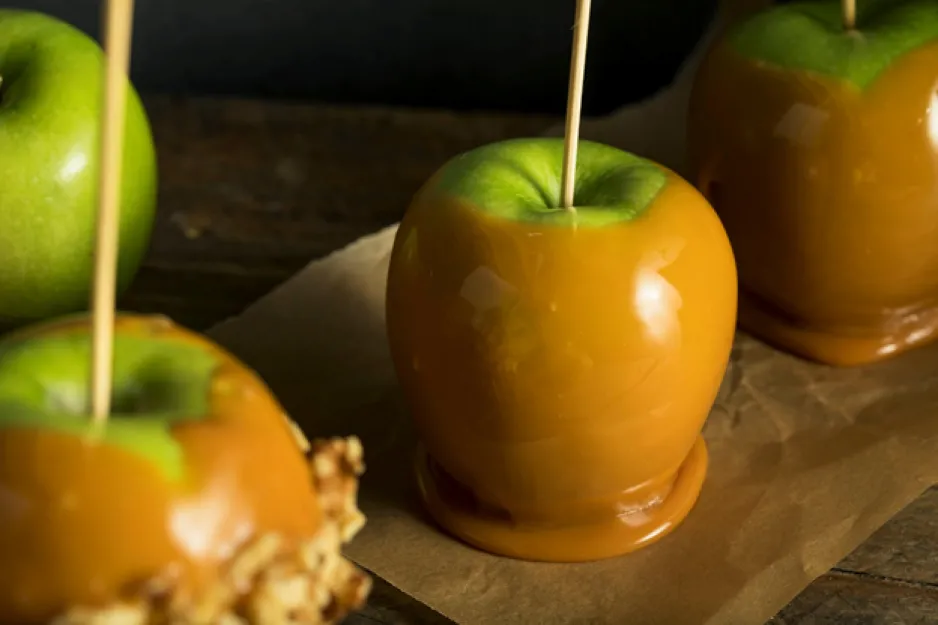 Green apples with wooden sticks in their centre, covered in caramel and laid out on a sheet of parchment paper.