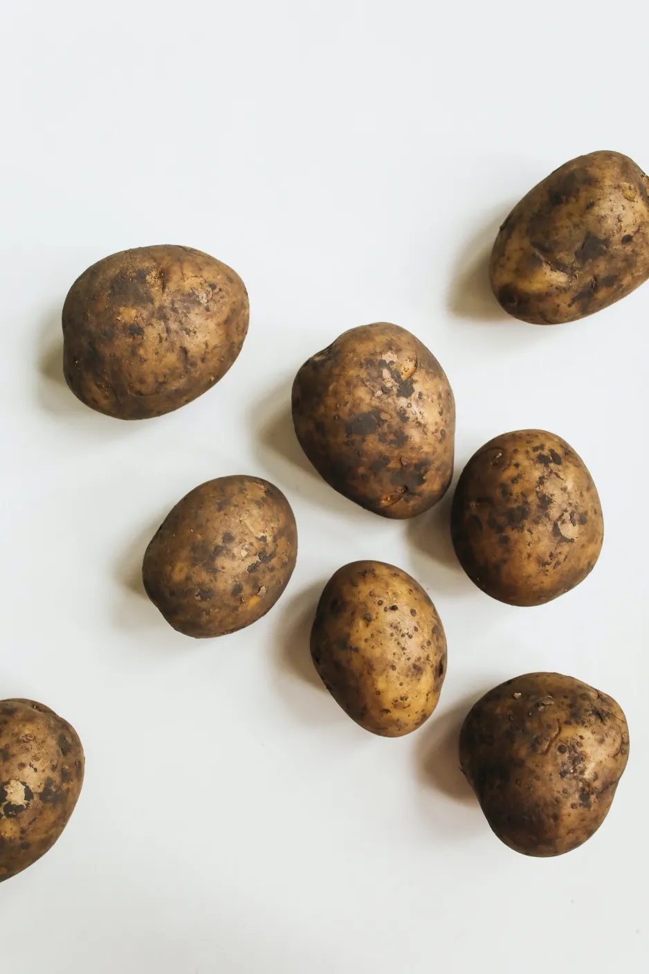 Several unwashed potatoes seen from above on a white background.