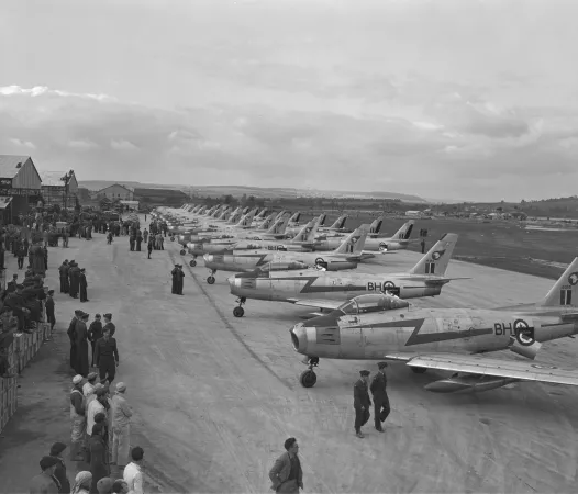 Black and white photo of many aircraft lined up on a runway. 