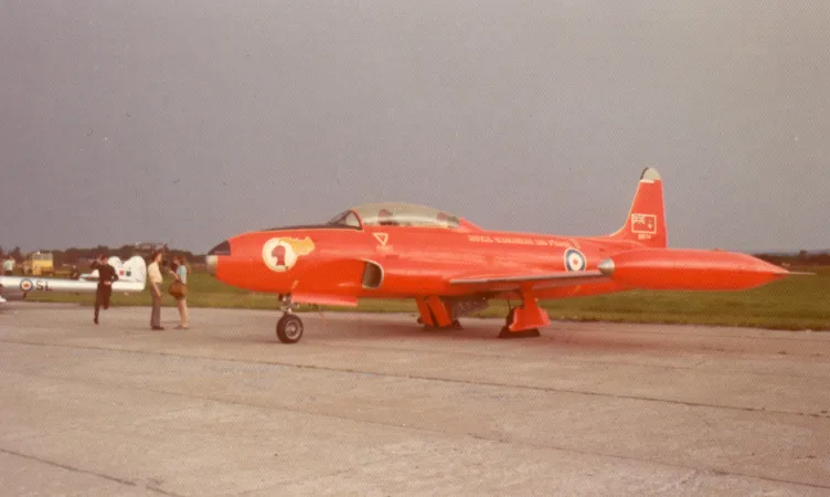 Avion à réaction orange vif aux formes arrondies immobilisé sur une piste d’aviation, photographié du côté gauche.
