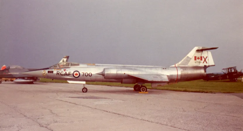 A streamlined, pointy-nosed silver jet airplane, photographed from the left side, sits on a runway.