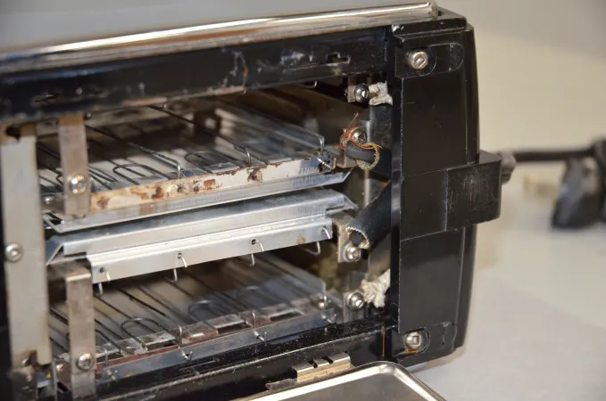  Bottom interior view of a silver and black toaster. The two bread slots are visible as well as asbestos coated cords with fraying edges.