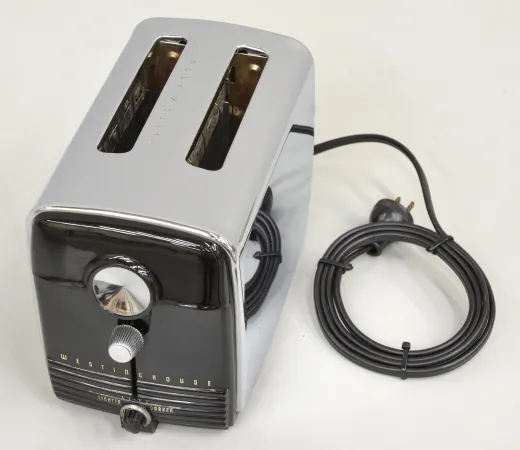 A close-up view of a toaster against a white background. The toaster has a black face with three knobs, and the body is silver; a black cord coming out from the back is rolled into a circle.