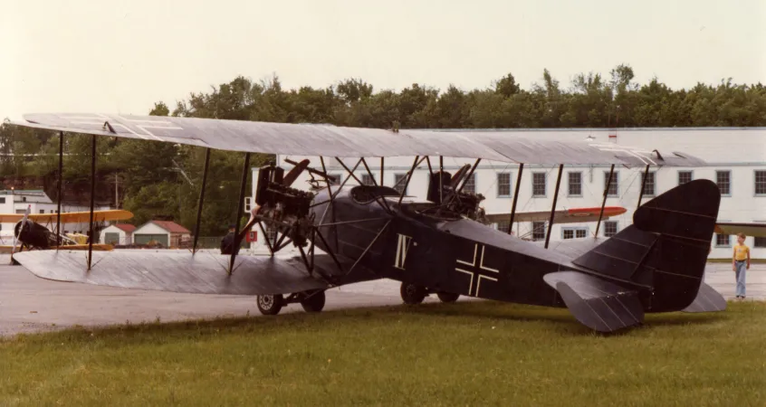 A large biplane, photographed outdoors from the back left, with a gray utilitarian building in the background.