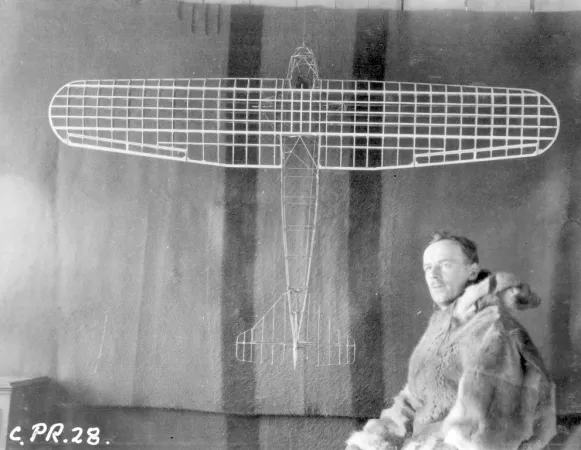 A member of the Hudson Strait Expedition sits beside a model aircraft. 