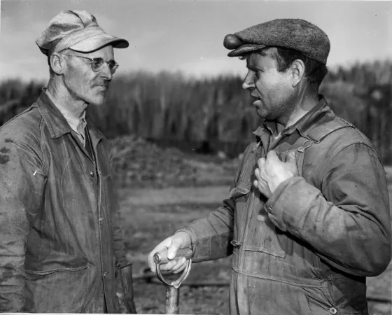 Two workers discuss  a day's outturn of iron ore from an emergency war mining project in Eastern Canada.
