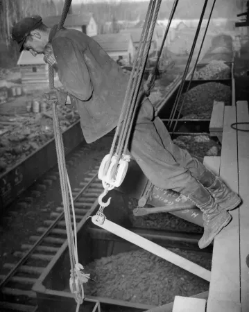 Un travailleur charge du minerai de fer dans les wagons d’un train du Canadien National pour un projet minier d’urgence en temps de guerre dans l’est du Canada.