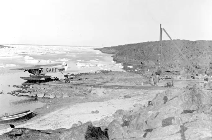 Black and white photograph showing an airplane being taken from the icy cove on a trolley