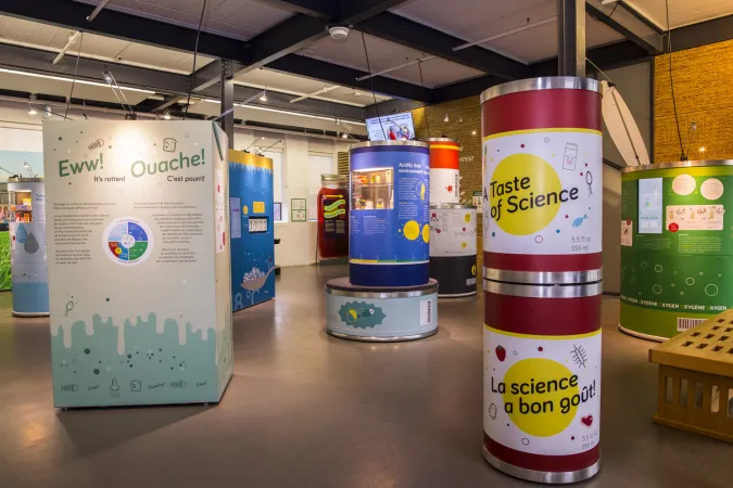 A wide shot of an exhibition showing many different modules of size, shape and colour. A white and blue rectangular module to the left has the word “Eww!” at the top of a graphic panel and a circular module with red and white bands has the title “Taste of Science.”