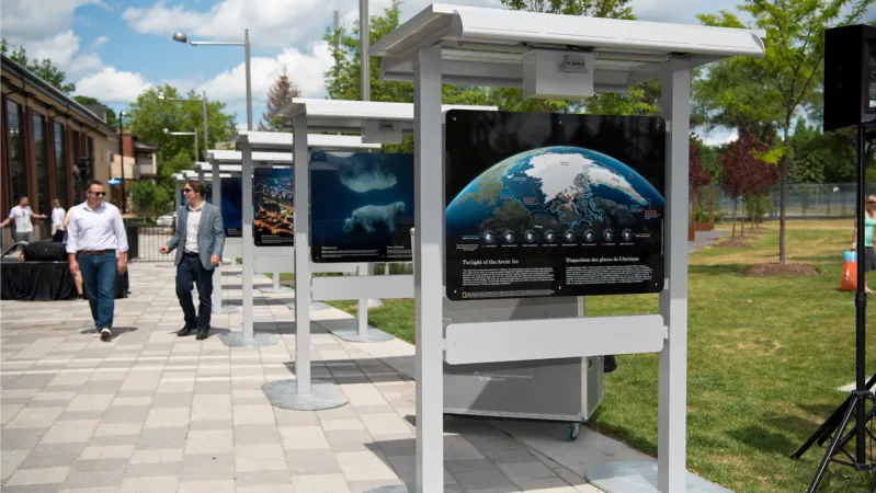 Two people walk alongside cascading photographic panels, in an outdoor setting.  The first panel has a photo of the earth from space with white text below.