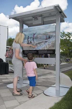 Une femme et un enfant regardent un panneau d’exposition, à l’extérieur.