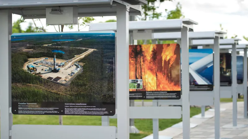 A wide shot of cascading exhibition photographic panels in an outdoor setting. The panel in the forefront is an aerial view of a factory in a forest setting.