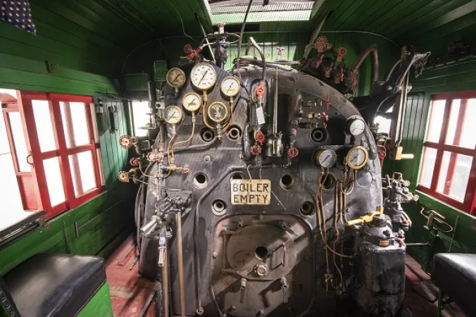 View of a locomotive’s boiler room, with a series of gauges and knobs.
