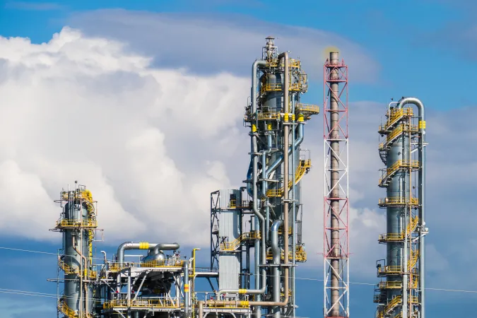 Towers of a nitrogen fertilizer production plant stand against a blue, cloudy sky.