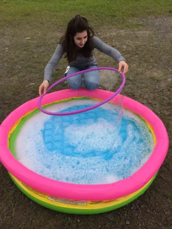 Intern Charlotte Clemens, attempting to make a giant bubble by pulling a hula hoop out of a kiddie pool. 
