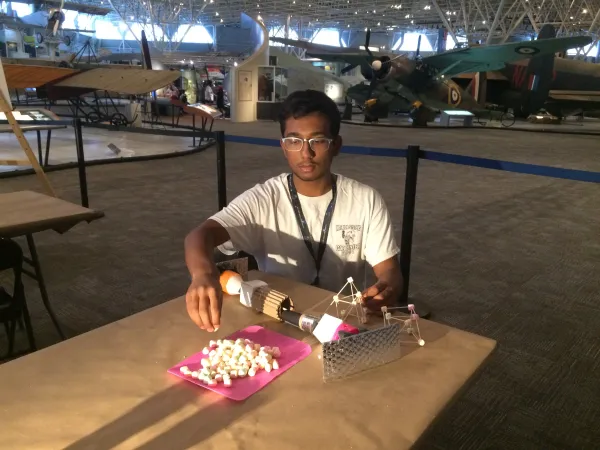 The author sits at a table and assembles a contraption using small marshmallows and other materials.