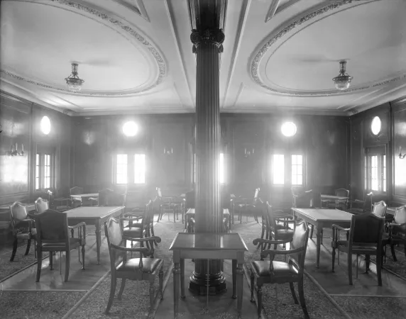 A black-and-white image of a formal dining saloon, filled with elegant tables and chairs.