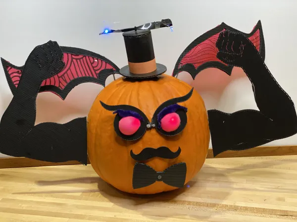 A pumpkin wearing a top hat, bow-tie, moustache, evil eyes, bat wings, and flexing two muscular arms. 