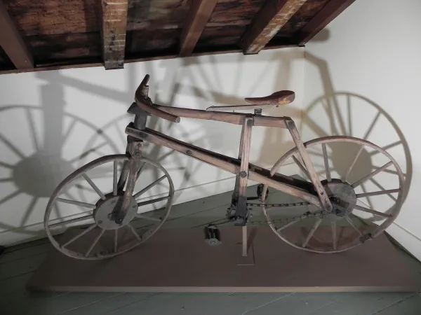 Trois photos représentant une bicyclette de bois dans un musée, avec sa chaîne et ses roues dentées.