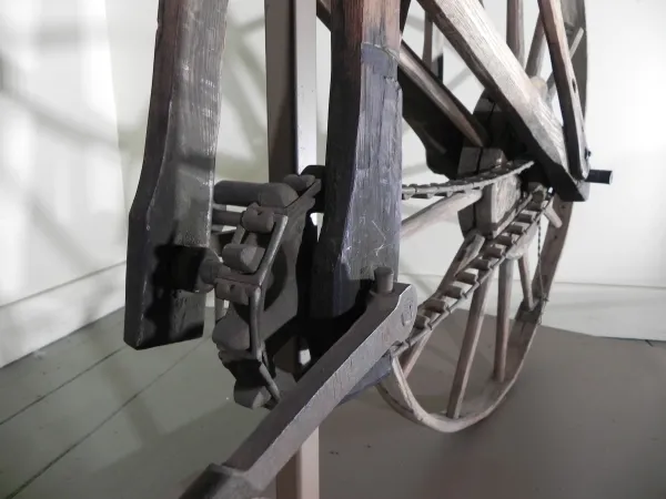 Three images in a gallery depicting a wooden bicycle and its chain and gears.