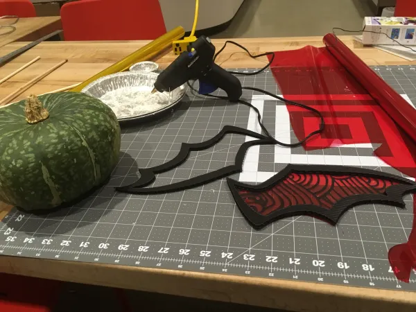 A workshop table covered in fabrics and cardboard, a glue gun, and a gourd. 