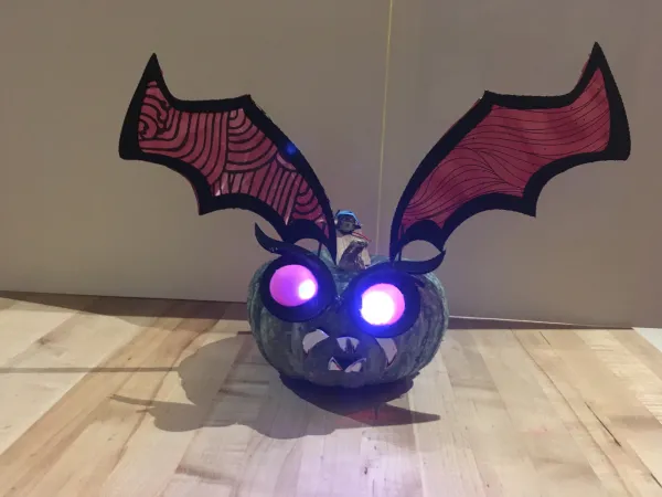A gourd with glowing eyes, giant pointy teeth, and red bad wings. 