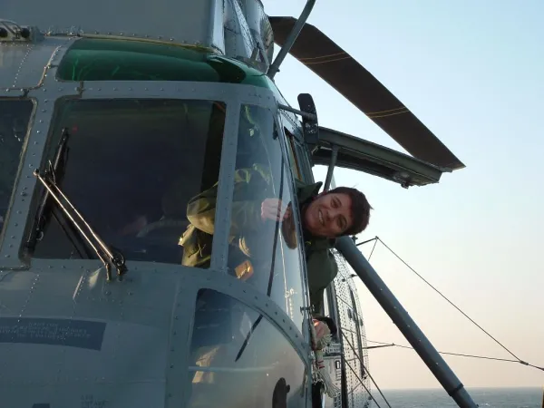 Une jeune femme vêtue d’un uniforme militaire vert sort la tête par la fenêtre latérale d’un aéronef.