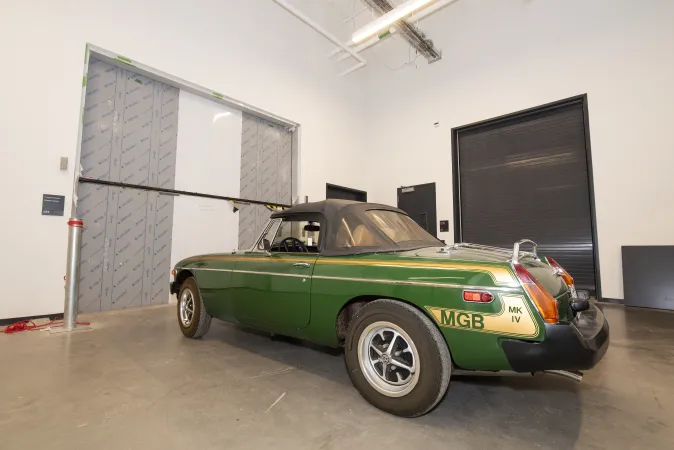 A green sports car sits outside of an oversized elevator door.
