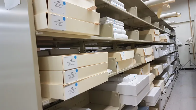 Photo showing shelves of boxes of archives as well as ledgers wrapped in white paper