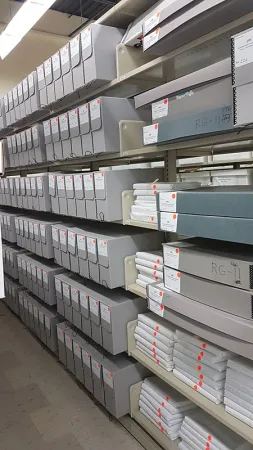 Photo showing more shelves of boxes of archives as well as ledgers wrapped in white paper