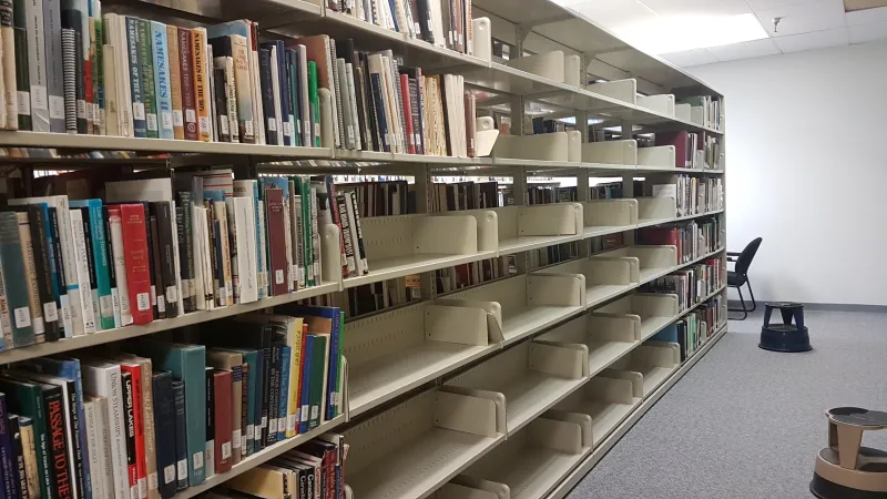 Photo showing a library shelf with some books, but nearly half-emptied for the packing