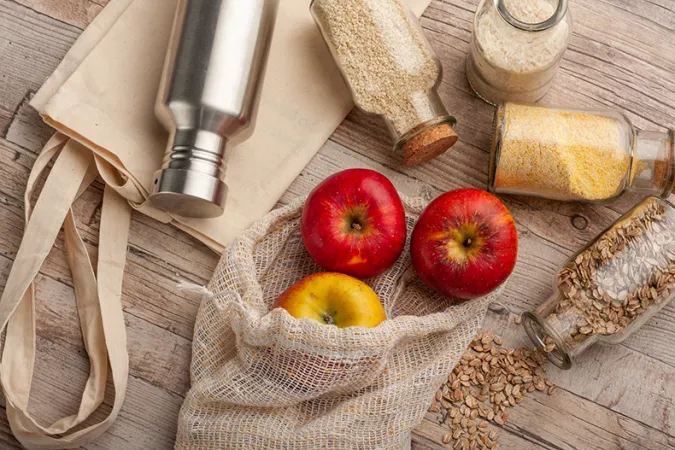 Red apples and various grains are pictured in reusable containers and cloth bags.