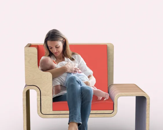 A young woman breastfeeds an infant on a modern-looking chair with an orange seat.