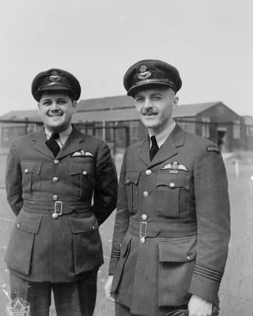 Une image en noir et blanc de David Hornell debout près de Denny Denomy. Les deux portent un manteau sur lequel sont épinglées des ailes de pilote.
