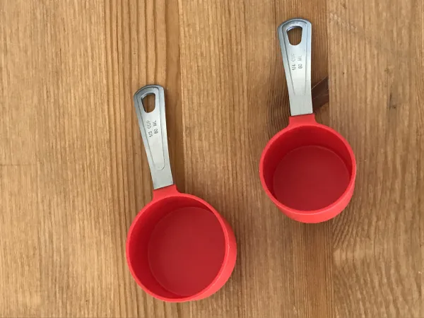 Deux petites tasses à mesurer en plastique rouge reposent sur une table en bois. 