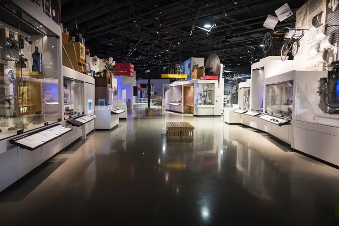 Une photo grand angle montre l’exposition L’Allée des artefacts du Musée des sciences et de la technologie du Canada. Une variété d’artefacts est visible dans des présentoirs des deux côtés de l’image.