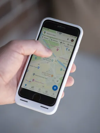 A close-up image shows a hand holding a smartphone; Google Maps is visible on the screen.