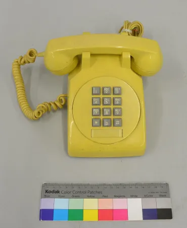Un téléphone de table brillant de couleur jaune vif et à pavé numérique gris repose sur un fond gris.