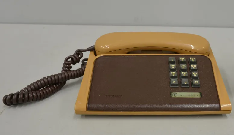 Un téléphone de table brun à clavier mat repose sur un fond gris après avoir été nettoyé.