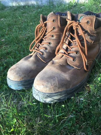 A pair of worn-in brown boots stand on a patch of green grass.