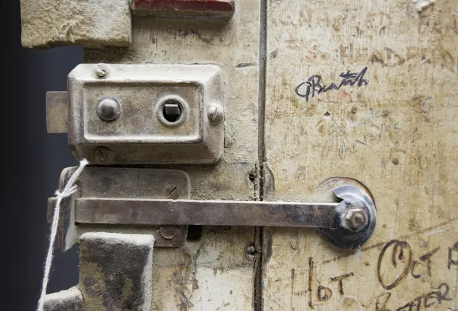 A close-up view of the latch of an old, wooden, graffiti-marked door.