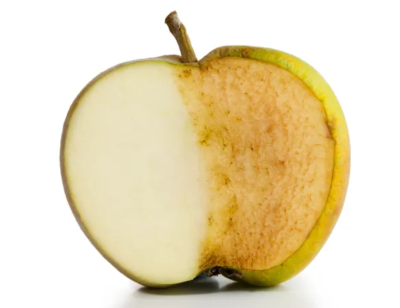 An apple with green skin is cut in half against a white background. Of the exposed apple, half of the face is white, the other is brown.