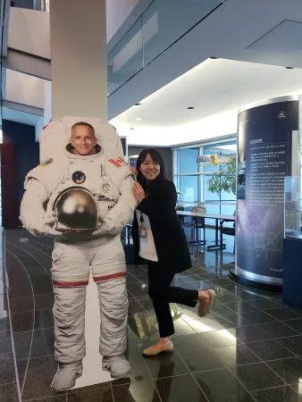 A young woman smiles and looks at the camera as she poses with a cardboard cut-out of Canadian astronaut David Saint-Jacques.