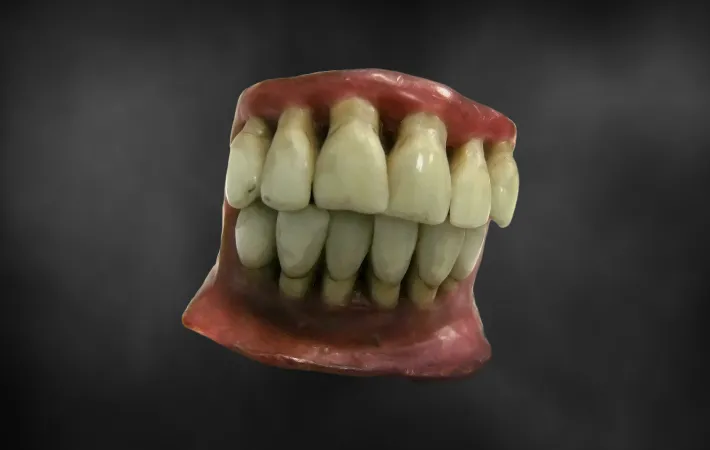 A wax model of a set of yellowed and unsightly teeth seem to be suspended in the air, set against a black background. 