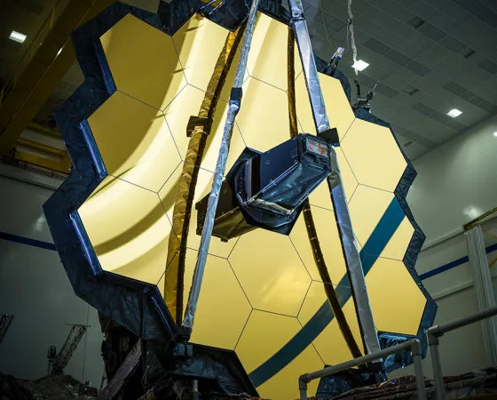 A close-up front view of the telescope’s primary mirror which resembles a golden honeycomb; a secondary mirror is folded up in front of it.