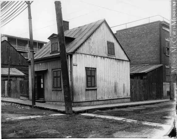 A black-and-white image depicts a wooden house in a working-class neighbourhood, early 1900s.