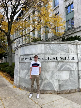 Le lauréat Jackson Weir est posé debout devant un gros mur de marbre portant l’inscription « Harvard Medical School ». À l’arrière-plan, on aperçoit un arbre et la façade d’un édifice.