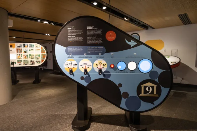 A large exhibition panel shaped like a rounded oval has dark blue graphics, three dials, and three circular screens.
