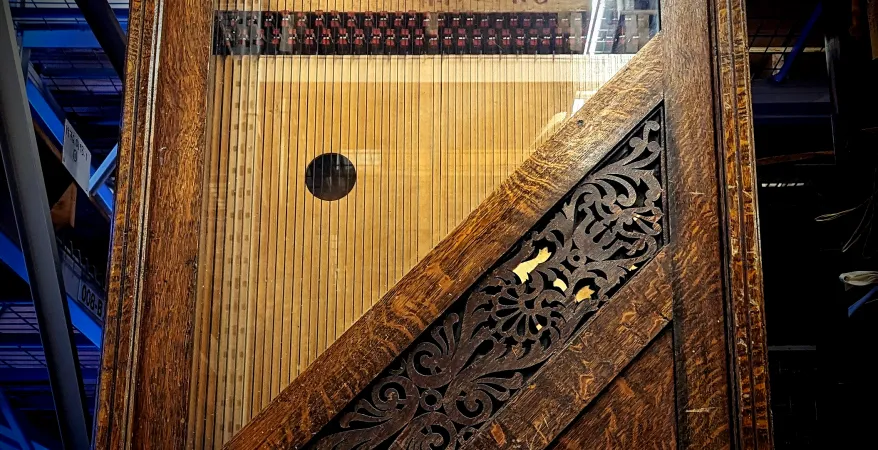 Close-up of Whitlock Automatic Harp in collections storage. Details show strings pulled across a wooden soundboard, encased behind a glass cabinet and framed by an ornate wooden cabinet.