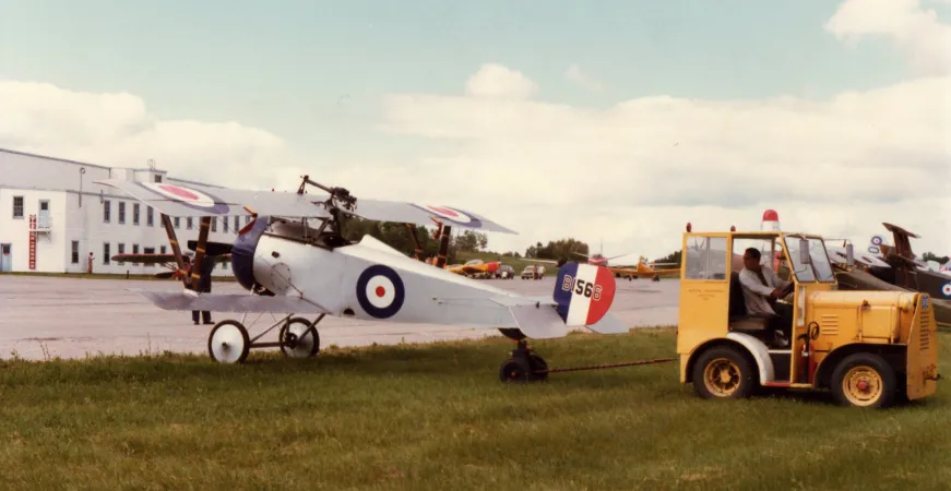 A small biplane is moved into place by a small yellow vehicle.